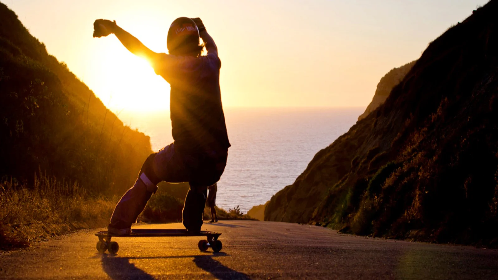 Longboarder carving a coastal road at sunset